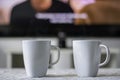 Coffee mugs with a television screen with a movie and subtitles in background