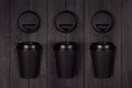 Coffee packing mockup - set fo three black paper cups and blank caps on dark black wood board, coffee shop interior. Royalty Free Stock Photo