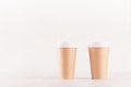 Coffee packing mockup - two kraft brown paper cups with white cap on white wood board with copy space, coffee shop interior. Royalty Free Stock Photo