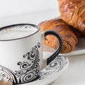 Coffee and pastries: a white coffee mug with a pattern, a silver spoon, fresh croissants on a saucer. Royalty Free Stock Photo