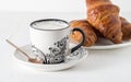 Coffee and pastries: a white coffee mug with a pattern, a silver spoon, fresh croissants on a saucer. Royalty Free Stock Photo