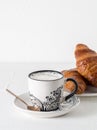 Coffee and pastries: a white coffee mug with a pattern, a silver spoon, fresh croissants on a saucer. Royalty Free Stock Photo