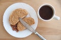 Coffee and peanut butter toasts on a white plate with a knife and peanuts. Wooden table. Top view