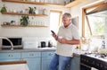 Coffee, phone and elderly man in kitchen texting and reading news or social media in his home. Happy, communication and Royalty Free Stock Photo