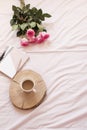 Coffee, pink roses, notebooks in bed on pink sheets. Freelance fashion home femininity workspace in flat lay style