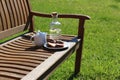 Coffee pitcher, glass bottle of homemade lemonade and cake on wooden bench, blurred green grass background. Outdoor