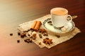 Coffee in a porcelain cup with a saucer, cinnamon, nutmeg and star anise on a jute napkin. Vintage coffee set on wooden table with