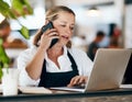 Coffee shop owner on a phone call while working online on her laptop inside a local cafe store. Contact us, learn about Royalty Free Stock Photo