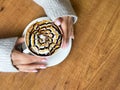 Coffee with spider web pattern on top of foam in white cup and girl& x27;s hands on wooden table background