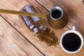 Coffee stands next to a white cup filled with hot coffee among scattered coffee beans, table, top view, horizontal