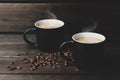 Coffee with steam. two black cups and grains of coffee on a dark woody background