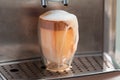 Coffee streaming from coffee machine and pouring out of glass full of milk foam Royalty Free Stock Photo