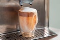 Coffee streaming from coffee machine and pouring out of glass full of milk foam Royalty Free Stock Photo
