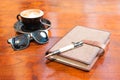 Coffee sun glasses pen and agenda on wooden table Royalty Free Stock Photo