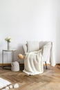 Coffee table with flowers near beige armchair with pillow and plaid