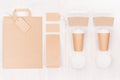Coffee takeaway set mockup for brand - two brown paper cups with blank bag, card, label, packet, sugar, cap on white wood board. Royalty Free Stock Photo
