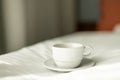 Coffee or tea cup on the bed. Hotel room or bedroom Interior, morning time. Concept of easy breakfast. One white ceramic Royalty Free Stock Photo