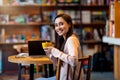 Coffee time. Happy young arab woman with mug of hot beverage, sitting in cafe and working at laptop computer Royalty Free Stock Photo