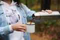 Coffee in travel. Girl pouring hot black coffee from thermos in white metal cup outdoor. Close up Royalty Free Stock Photo