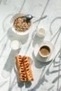 Coffee white cup, sweet rools and milk, oatmeal on gray background in sunlight ray, selective focus. Breakfast concept, shadow,