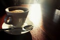Coffee in white cup on wooden table in morning sunlight. Morning aroma coffee concept. White cup with plate and spoon in sunlight. Royalty Free Stock Photo