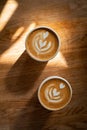 Coffee on wooden background. Two cups of cappuccino with latte art on brown table with sunbeam. Fresh morning coffee Royalty Free Stock Photo