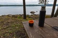 Coffeecup and a thermos at a table near a lake Royalty Free Stock Photo