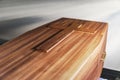 Coffin, funerary wooden brown box in an empty room. Might be in a funeral, burial, church or hospital. There`s a cross on top