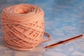 A coil of large knitted yarn of peach color with orange shiny hook on the surface of blue marble