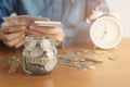 A coin in a glass bottle Image blurred background of business people sitting counting money and a retro white alarm clock,