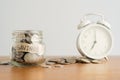 A coin in a glass bottle, a pile of coins and a white retro alarm clock on a brown wooden table. Investment business, retirement, Royalty Free Stock Photo