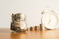 A coin in a glass bottle, a pile of coins and a white retro alarm clock on a brown wooden table. Investment business, retirement, Royalty Free Stock Photo