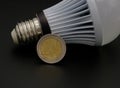 A coin leaning against a light bulb ,on a black background. Concept of blackout and expensive bill Royalty Free Stock Photo