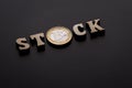 Coin of one euro among the wooden letters that make up the word STOCK. Black texture background. Shallow depth of field. Close-up