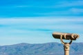 Coin operated binocular telescope for distant viewing. Blurred range of green hills, mountains in the distance under cloud sky Royalty Free Stock Photo