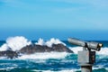 Coin operated monocular telescope for distant viewing. Blurred ocean background with giant waves crashing over coastal rocks and Royalty Free Stock Photo
