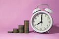 Coin pile stacked with alarm time clock with sweet pink space background for times to saving money concept