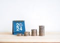 Coin stack as a growth graph with up arrows near 2024 desk calendar on wooden table and white background.