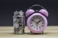 Coins in a clear glass jar with vintage clock nearby. Saving is money saved for education