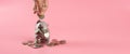 Coins in glass bottle put on table with hand putting money coins pink background.