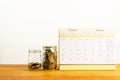 Coins in glass jar and calendar on wooden table for saving,accou