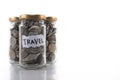 Coins in a glass jar labeled ` TRAVEL ` on a white background. Royalty Free Stock Photo
