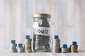 Coins and glass jar on a table with miniature house, with a note written ` HOUSE `. Royalty Free Stock Photo