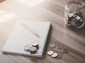 Coins money with blank white notebook on wooden table and sunlight background, finance and banking business finance concept. Royalty Free Stock Photo