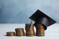 Coins and student graduation hat on wooden table against blue background. Tuition fees concept Royalty Free Stock Photo