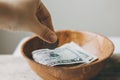 Hand putting Coins in a wooden bowl, donate and give concept.