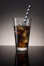 Cola with rum and ice in a glass with a striped tubule.