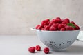 Colander with delicious ripe raspberries on table against light background, space for text