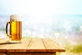 Cold beer in big glass on wooden table with ocean and sandy beach background. Copy space for advertising product. Royalty Free Stock Photo