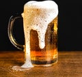 Cold beer with foam in a mug, on a wooden table and a dark background with blank space for a logo or text. Stock Photo mug of cold Royalty Free Stock Photo